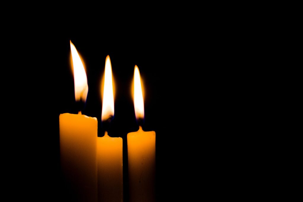 Three lit candles with bright flames are arranged closely together against a completely black background, creating a warm and peaceful glow for the Robert L. Mason Jr. Candlelight Memorial.